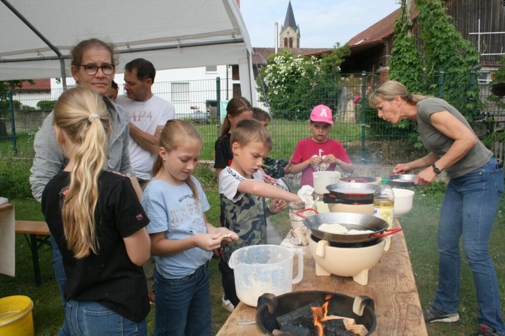Kinder stehen an den Zwergenfeuern und machen Pfannenbrot