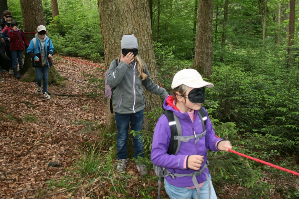 Kinder hangeln sich mit Augenbinden am roten Seil entlang