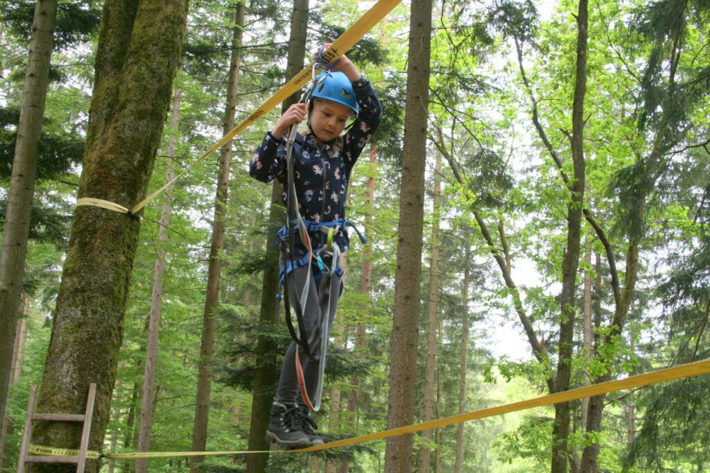 EIn Mädchen gesichert auf dem Hochseil zwischen zwei Bäumen