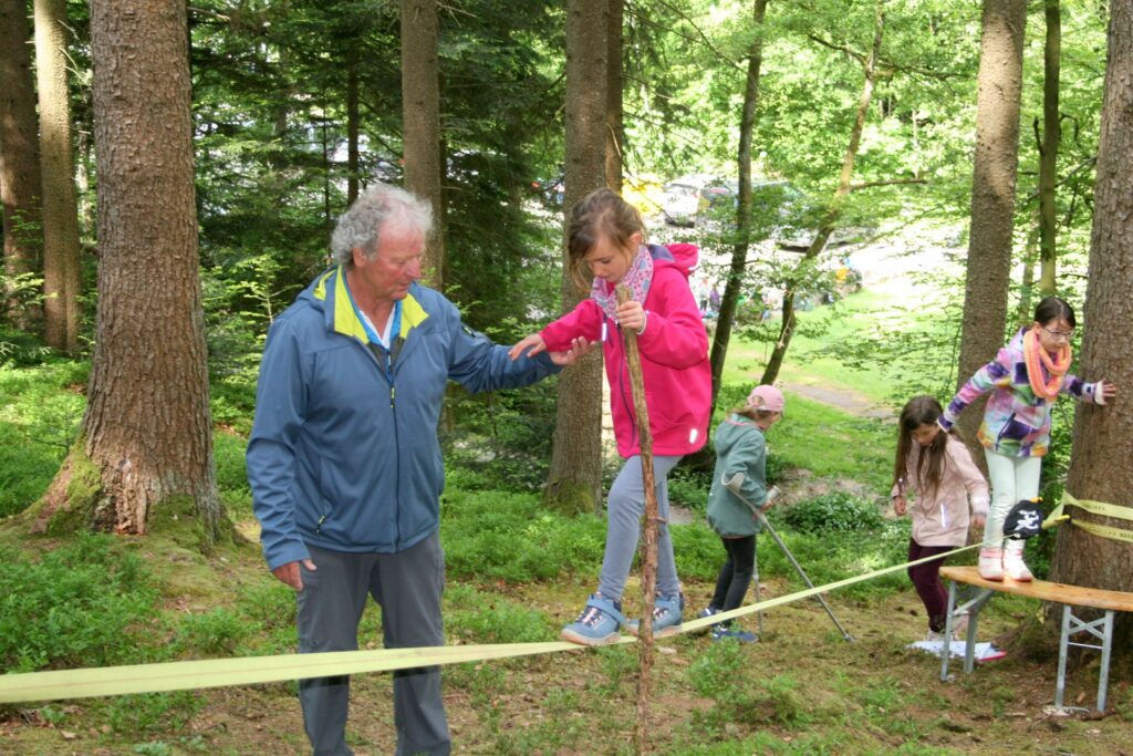 Ein Kind auf der Slackline zwischen Bäumen wird an der Hand geführt