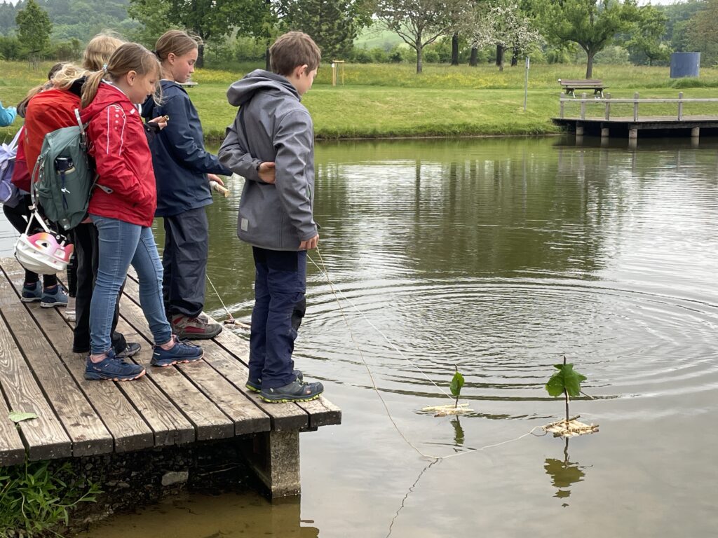 Die Kinder stehen auf dem Steg und lassen ihre Floße schwimmen