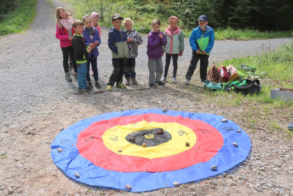 Eine Gruppe Kinder steht beim Waldsporttag vor der Zielscheibe für den Tannenzapfenzielwurf.