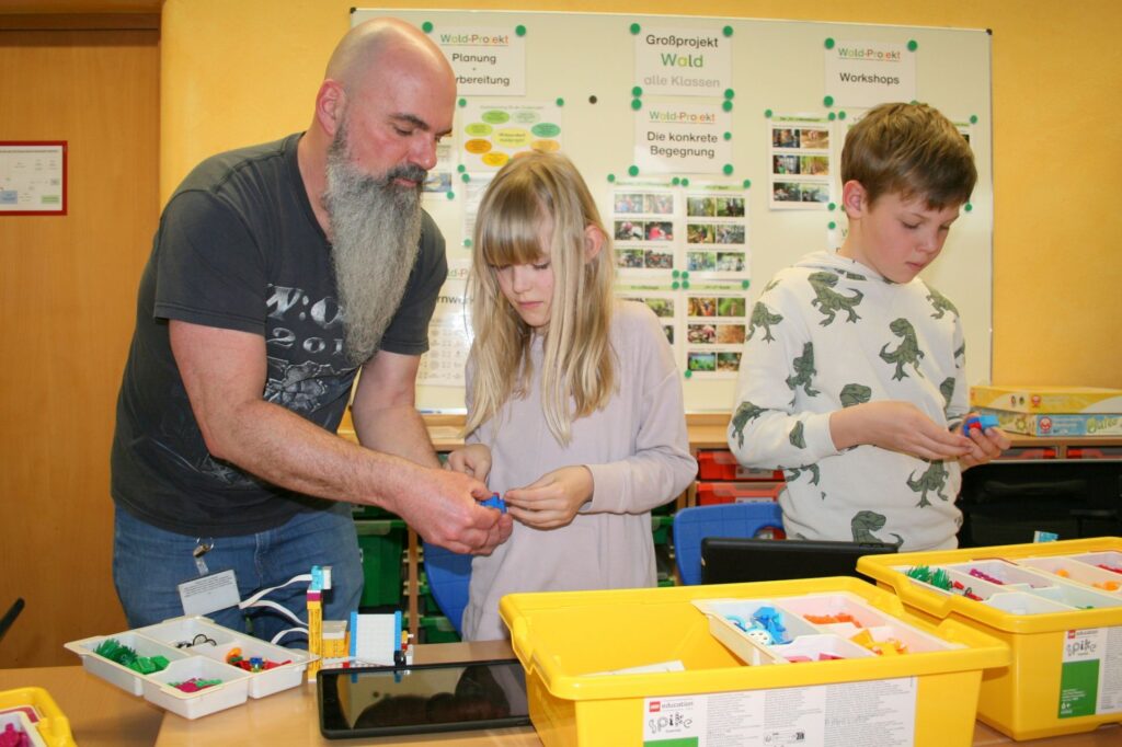 Herr Pfauser hift zwei Kindern beim Bau der LegoRobotik- Modelle