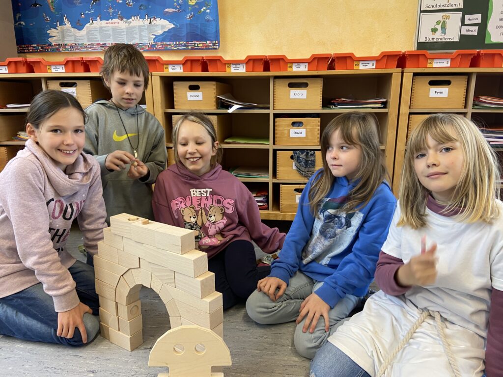 Fünf Kinder sitzen um den römschen Bogen aus Holzklötzen