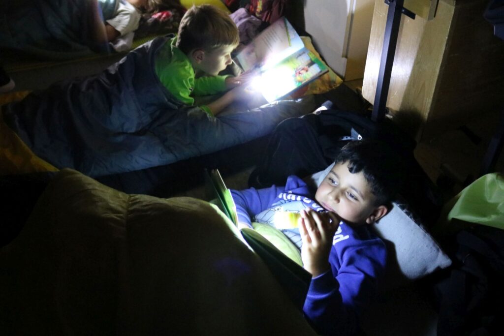 Die Kinder lesen mit Taschenlampen gemütlich in ihren Schlafsäcken.