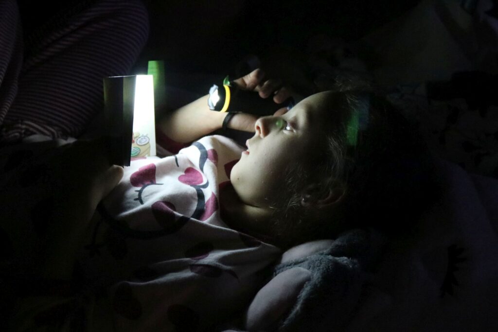 Nahaufnahme eines Mädchens mit Taschenlampe und Buch.