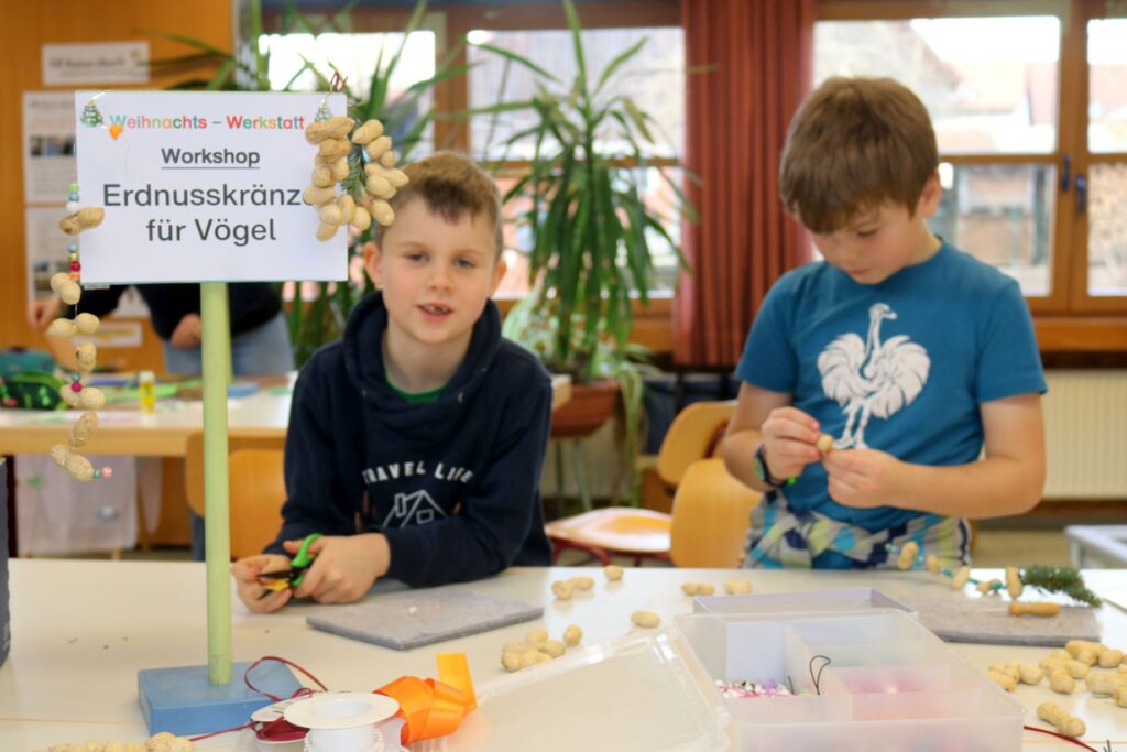 Zwei Jungen fädeln Erdnüsse für die Vögel auf.