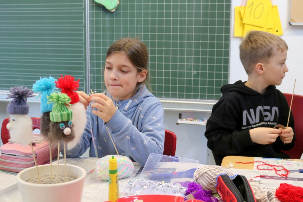 Ein Mädchen und ein Junge stellen Weihnachtswichtel- Stecker her.