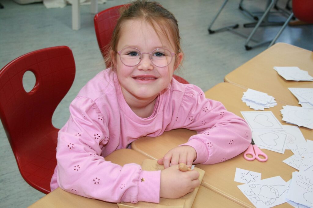 Ein Mädchen prickelt die Löcher in ihr Windlicht aus einer Papiertüte.
