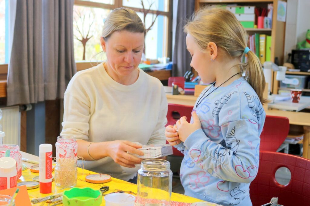Eine Mutter ist einem Mädchen beim Windlicht gestalten behilflich.