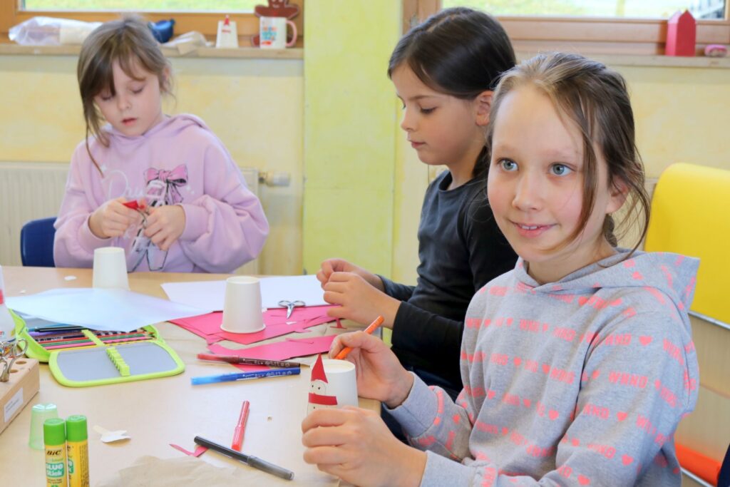 Drei Mädchen basteln einen drehbaren Stimmungsschneemann aus Pappbechern.