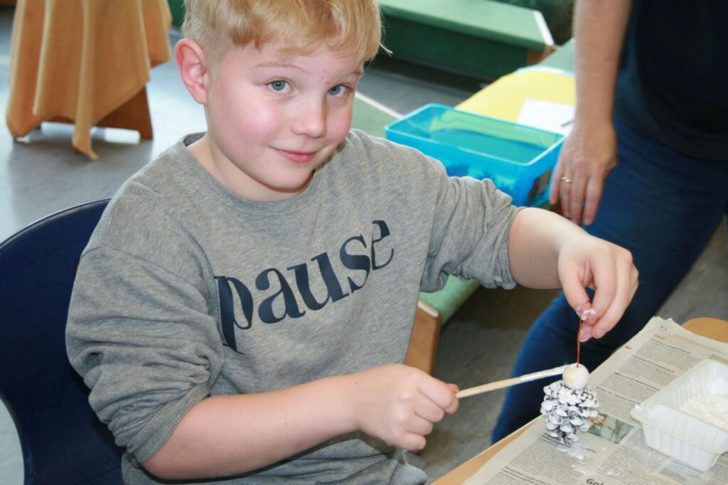 Ein Junge beim Bemalen von Zapfen für Engel und Schneemänner.