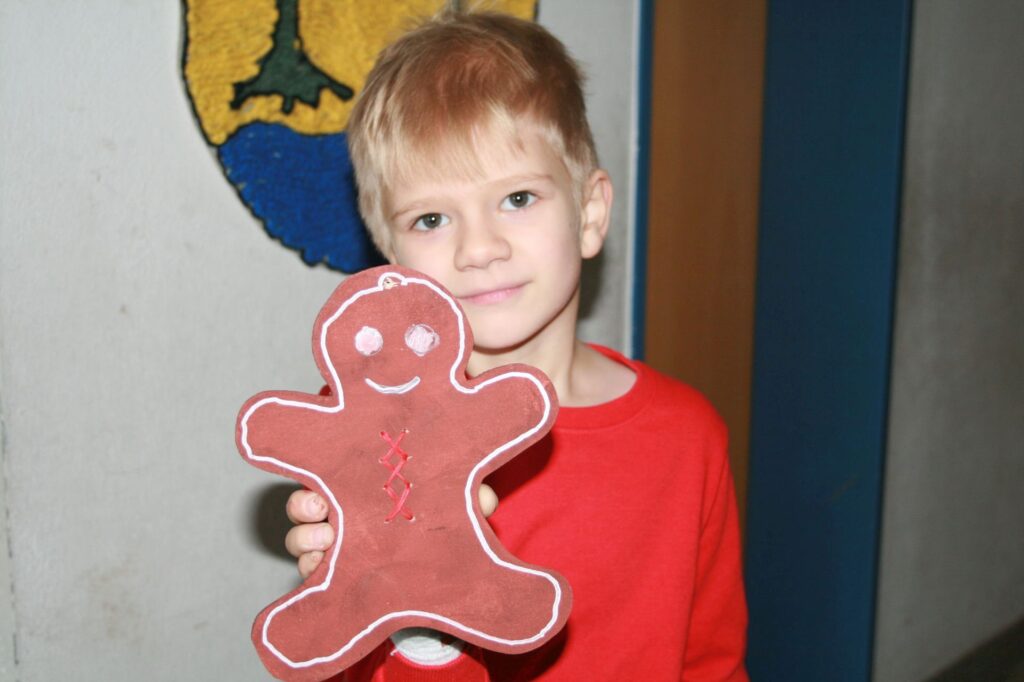 Ein anderer Junge präsentiert seinen fertig bemalten Lebkuchenmann aus Holz.
