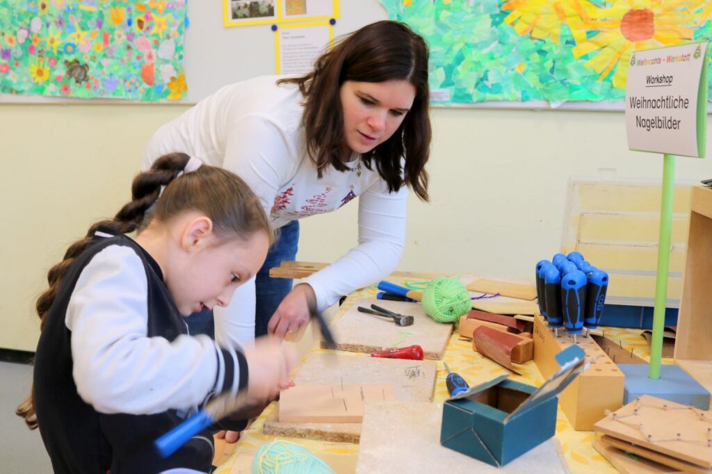 EIne Mama unterstützt ein Mädchen beim Nageln eines Sterns.