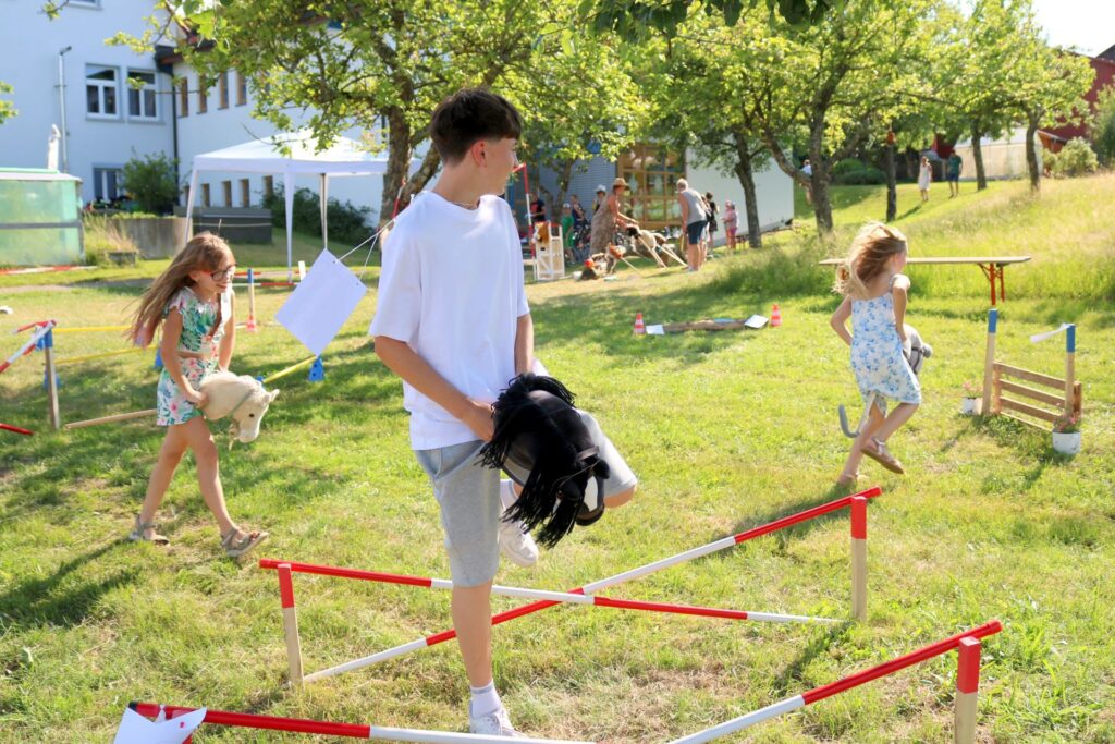 Kinder hüpfen mit Steckenpferden über Hindernisse
